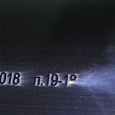 Close-up of a metal surface with laser-etched text '018 p.19-1°' surrounded by a smoky effect.